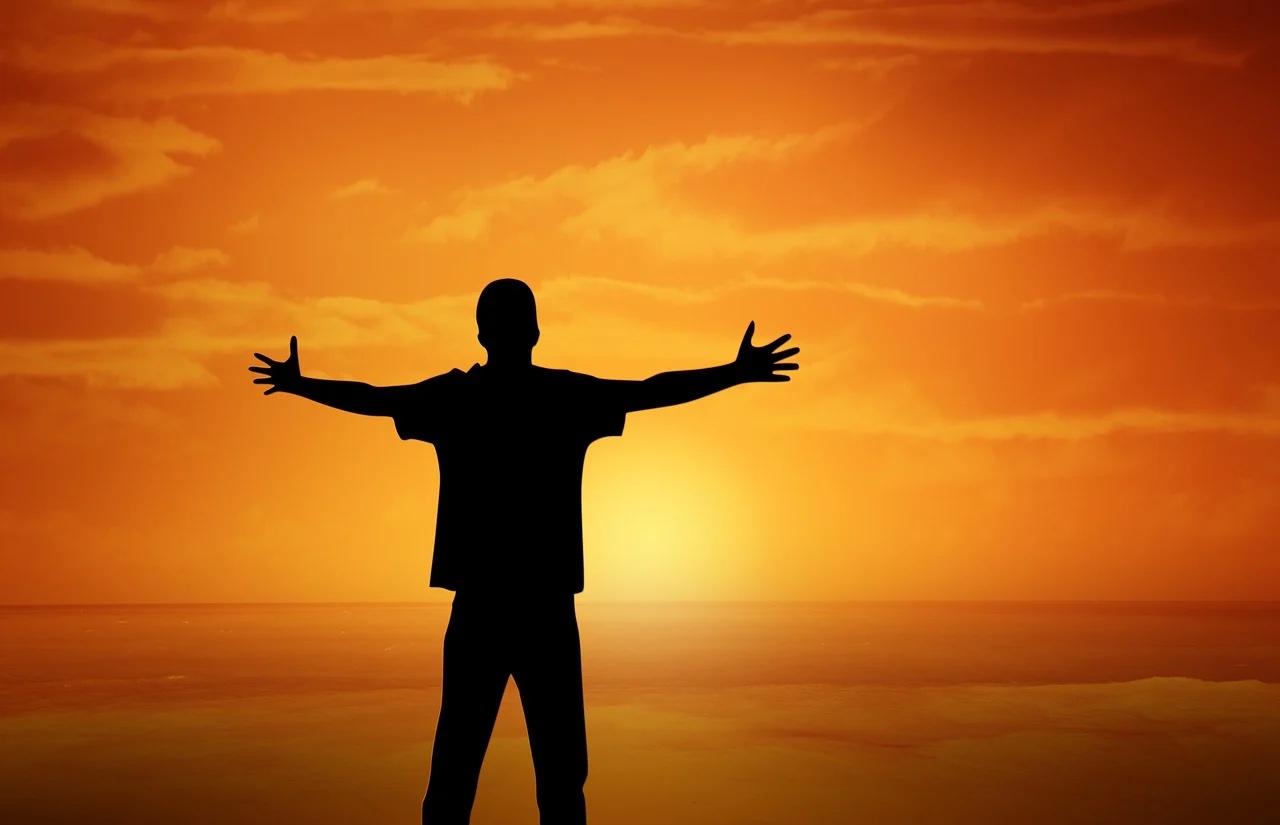 foto di un uomo con le braccia in segno di apertura che guarda il sole